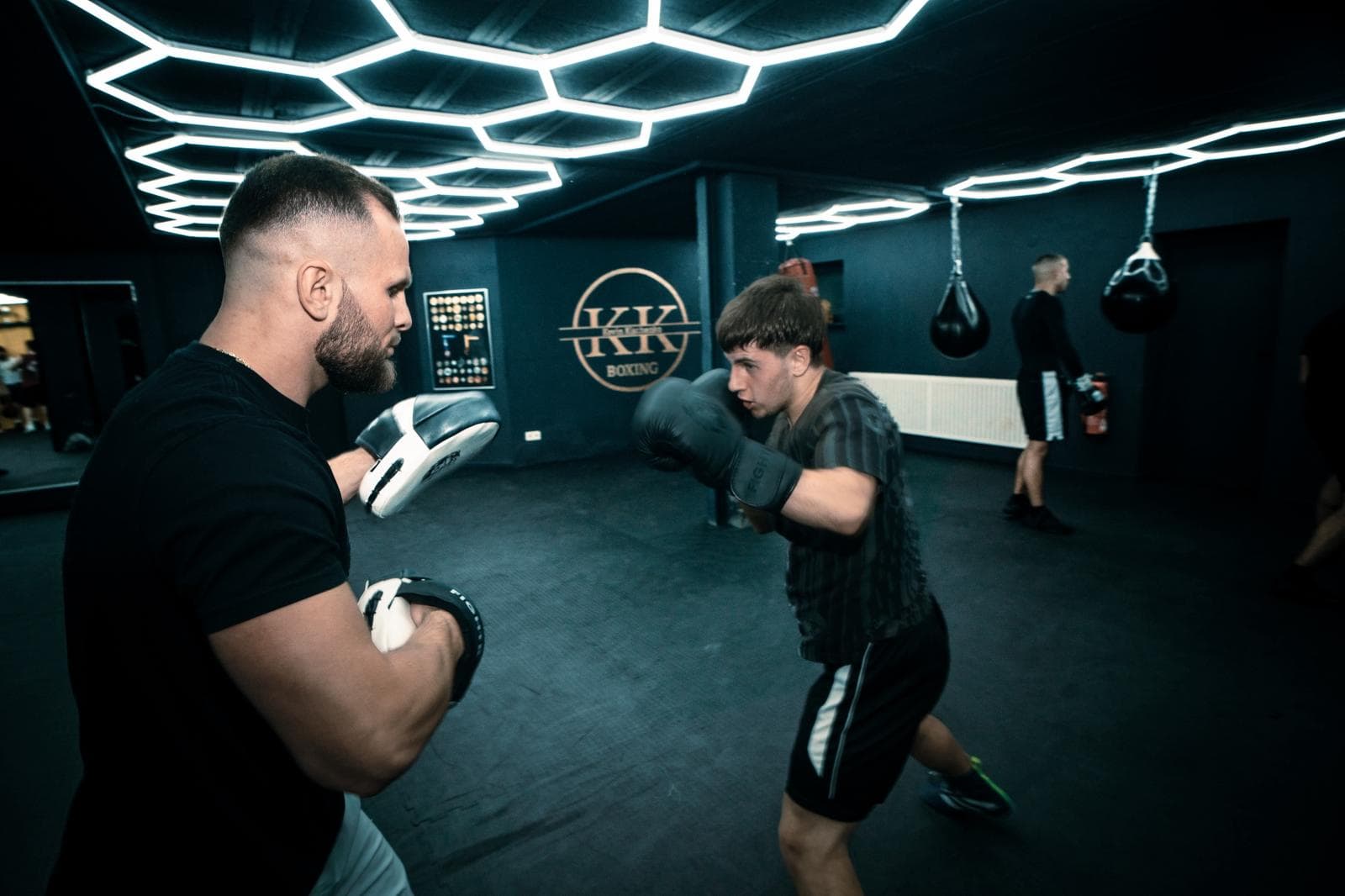 Kevin hält einem jungen Boxer die Pratzen, im Hintergrund KK-Logo und zwei Tropfensäcke